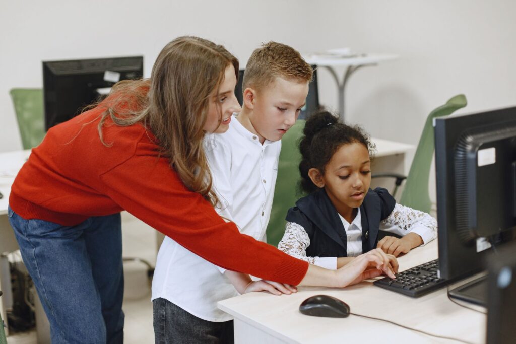Teacher helping students at computers, showing why classroom awareness matters in extended reality vs virtual reality choices